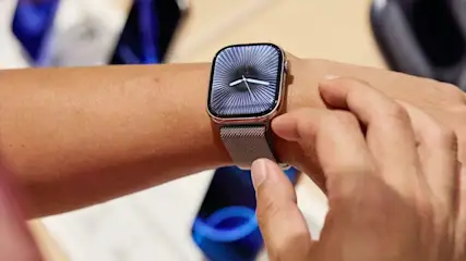 Person traegt eine moderne Smartwatch mit silbernem Armband am Handgelenk und bedient das Display mit dem Finger.