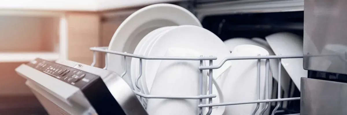 Offener Geschirrspüler mit weißem Geschirr in grauem Korb. Links ist das Bedienfeld sichtbar, dahinter eine helle Küche.