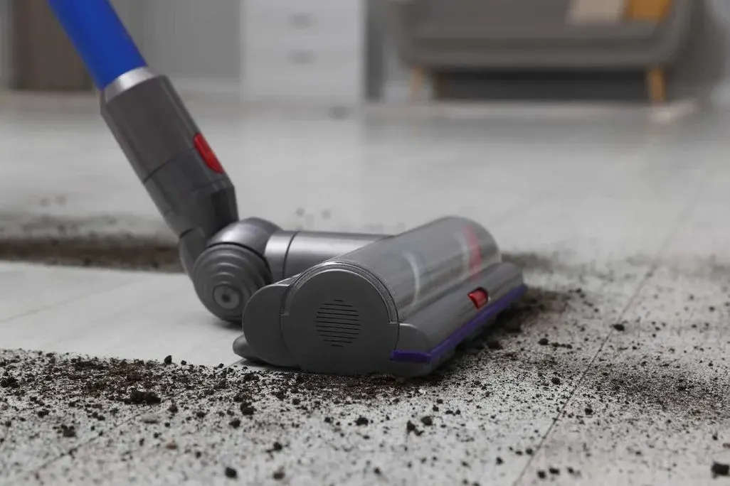 Kabelloser Staubsauger mit blauem Griff reinigt Bodenfläche von Staub und Schmutz.
