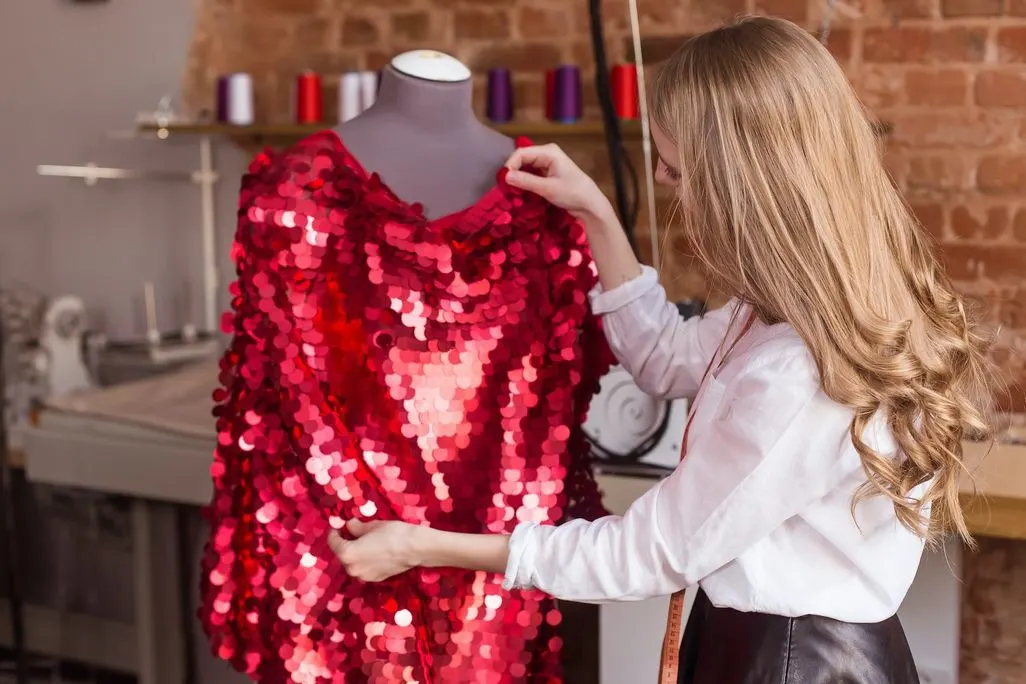 Frau legt ein rotes Pailettenkleid auf eine Schneiderbueste in einem Atelier