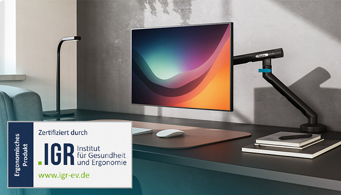 Ein schwarzer, flexibler Digitus Monitorarm ist an einem modernen Schreibtisch montiert und hält einen Flachbildschirm. Unten links ist das Siegel "Ergonomisches Produkt" vergeben vom IGR (Institut für Gesundheit und Ergonomie) eingeblendet.