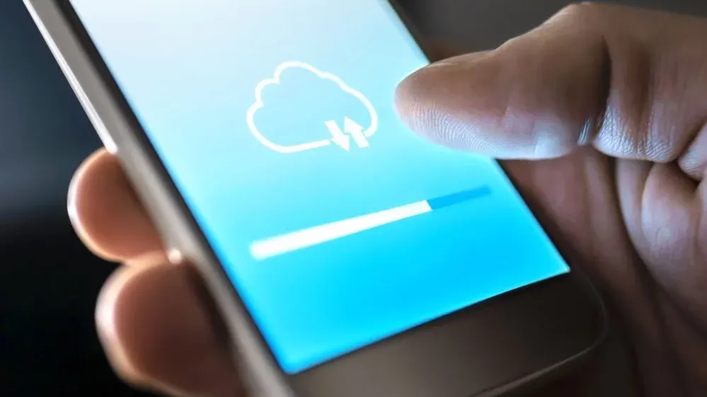 Eine Hand hält ein Smartphone mit blauem Bildschirm. Ein weißes Cloud-Symbol mit Pfeilen und eine Fortschrittsanzeige sind zu sehen.