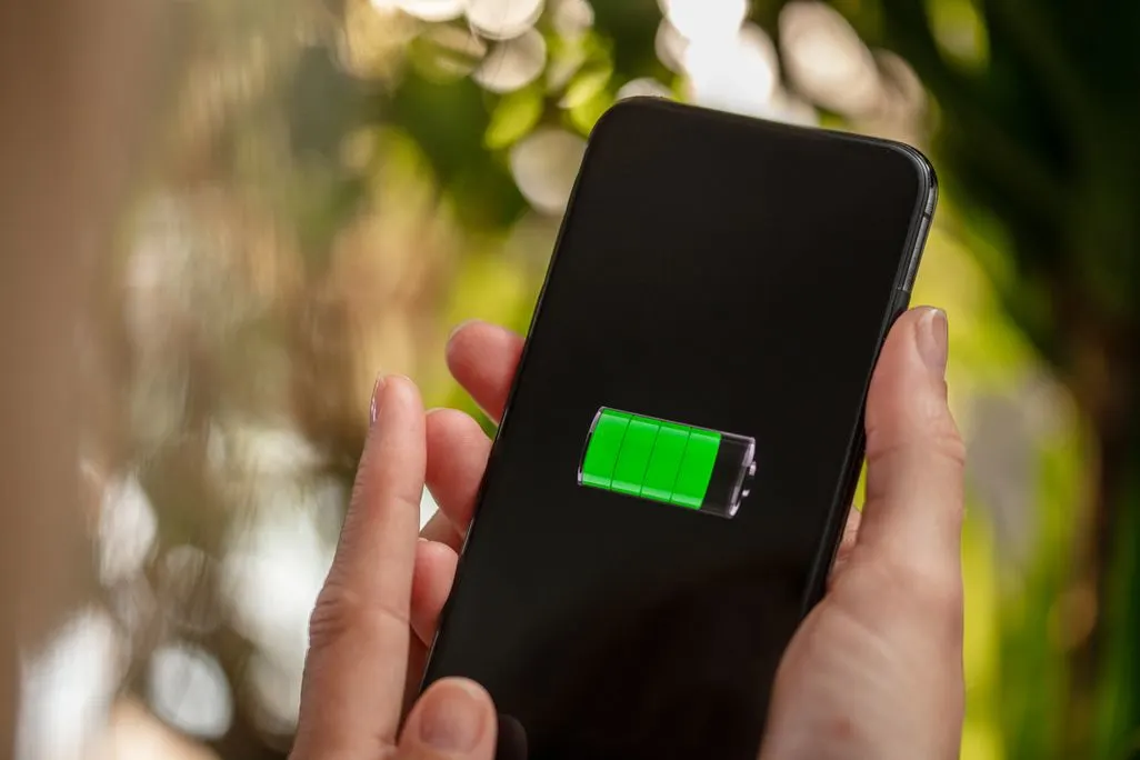 Smartphone mit grüner voll geladener Batterieanzeige auf dem Bildschirm wird von zwei Händen gehalten.