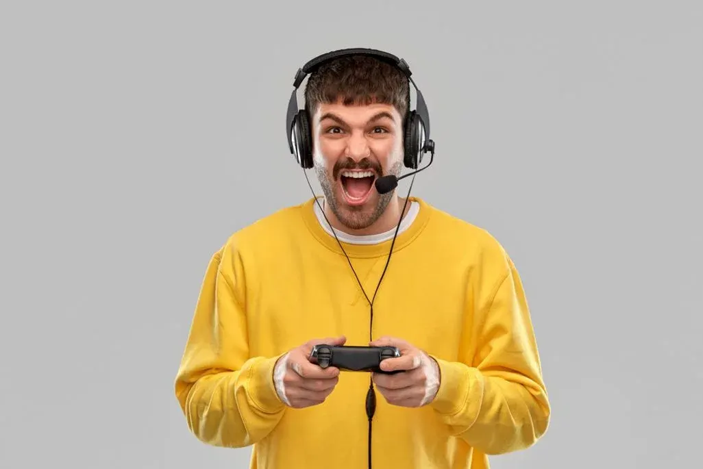 Mann mit gelbem Pullover trägt Headset und spielt mit Controller