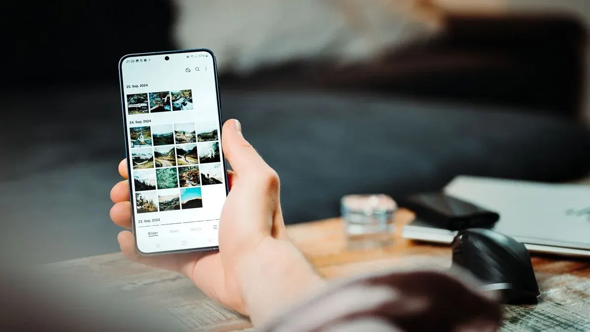 Hand hält Smartphone mit geöffneter Galerie-App über einem Schreibtisch.