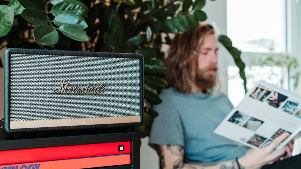 Ein Marshall Lautsprecher steht auf einem Regal, im Hintergrund sitzt eine Person und liest.