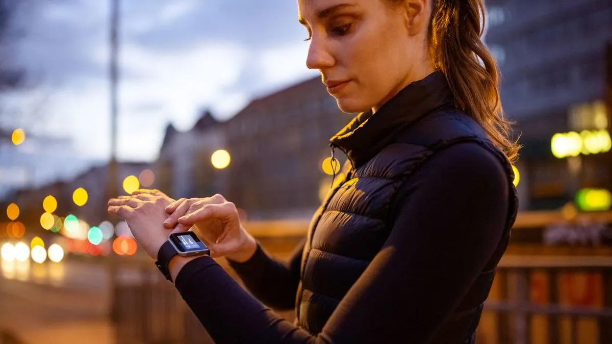 Eine Frau bedient eine Smartwatch beim Joggen in der Stadt am Abend.