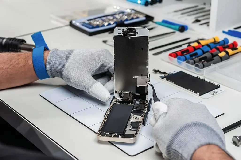 Feinmechaniker entfernt mit einer Pinzette eine Platine aus einem geoeffneten Smartphone