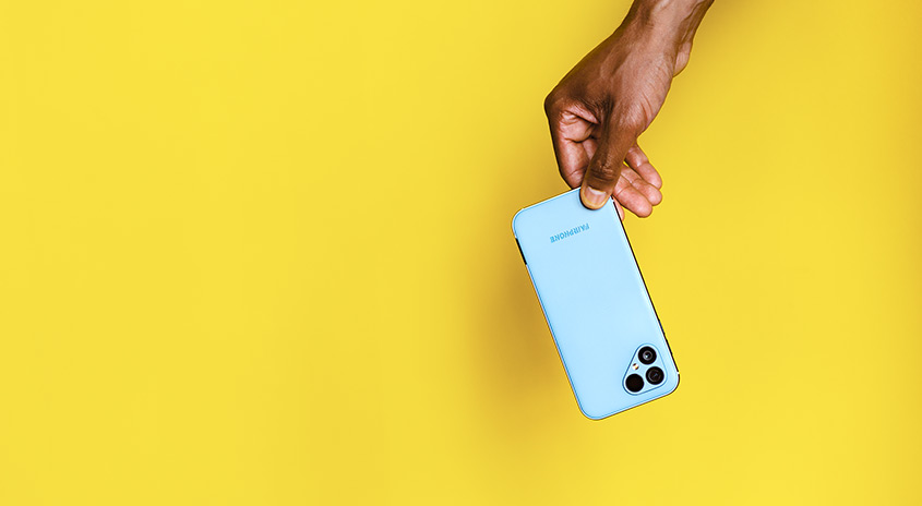 Eine Hand hält ein hellblaues Smartphone vor einem gelben Hintergrund. Die Kamera ist sichtbar.