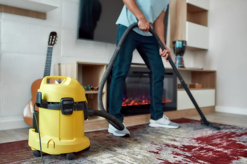 Person saugt mit gelbem Nass-Trockensauger einen bunten Teppich im Wohnzimmer