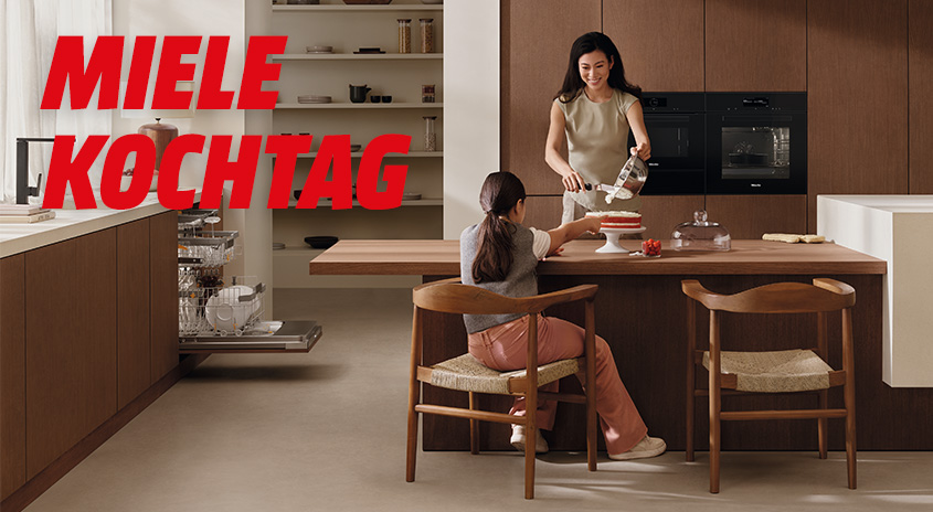 Eine Küche mit braunen Schränken, einem Geschirrspüler und einem Holztisch mit Stühlen. Auf dem Tisch steht Essen.