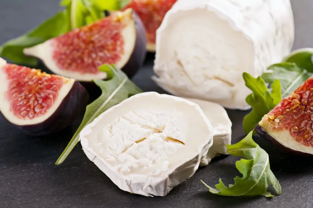 Ziegenkäse und frische Feigen mit Rucola auf dunklem Untergrund angerichtet.