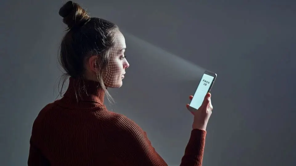 Eine Frau entsperrt ihr Smartphone per Face-ID, ein Raster über ihrem Gesicht veranschaulicht den Vorgang.