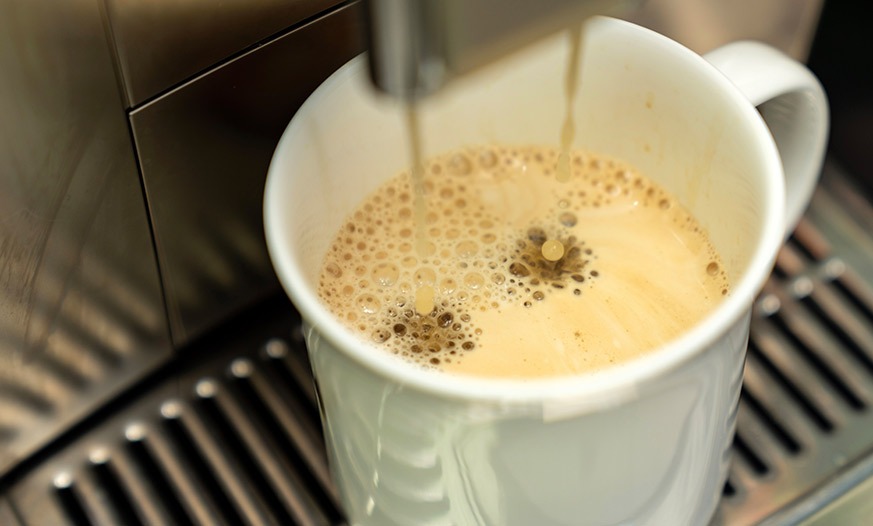 Kaffeetasse steht unter dem Kaffeeauslass eines Kaffeevollautomaten und wird befüllt.