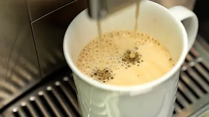 Kaffeetasse steht unter dem Kaffeeauslass eines Kaffeevollautomaten und wird befüllt.