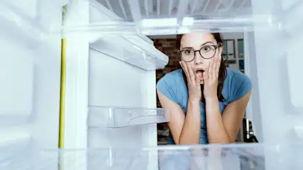 Frau schaut entsetz in eine defekten Kühlschrank