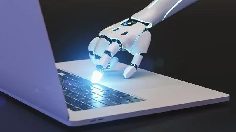 Eine weiße Roboterhand mit blauen Lichtern drückt eine leuchtende Taste auf der Tastatur eines weißen Laptops.