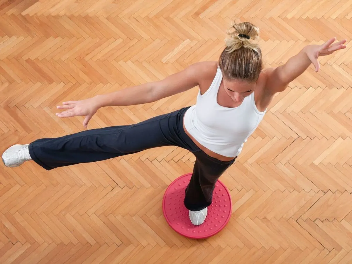 Eine Frau in Sportkleidung macht eine Übung auf einem Balanceboard.