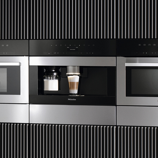 Nahaufnahme einer eingebauten Miele-Kaffeemaschine mit Tasse. Die Maschine ist in einem schwarzen Schrank mit silbernen Akzenten platziert.