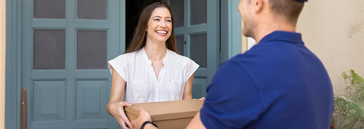 Frau steht vor offener Haustür und übernimmt ein Paket von einem Paketboten.