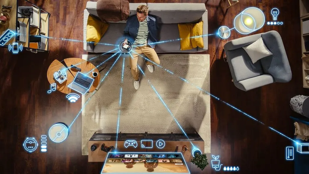 Ein Mann sitzt im Wohnzimmer und steuert verschiedene smarte Geraete mit dem Smartphon
