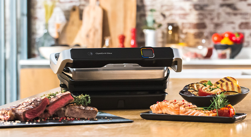 Ein Tisch mit einem schwarzen OptiGrill, gegrilltem Steak, Lachs und Gemüse in einer Küche.