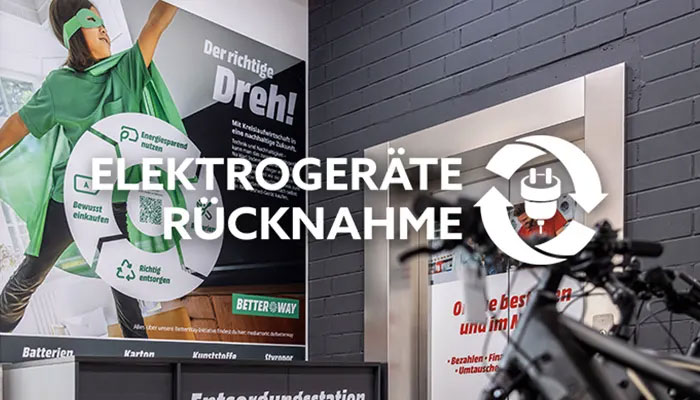 Plakate zur "Elektrogeräte Rücknahme" und "Entsorgungsstation" vor einer grauen Backsteinmauer. Ein Fahrrad ist teilweise sichtbar.