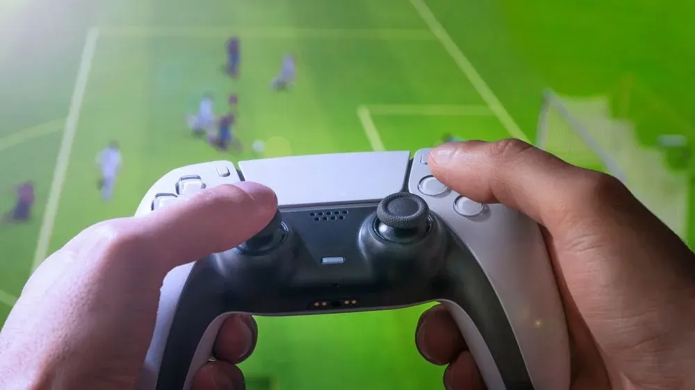 Zwei Hände halten einen weiß-schwarzen Gamecontroller, Daumen auf Joysticks, Zeigefinger auf Tasten.