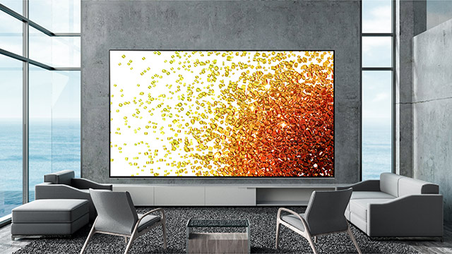 Graue Sofas und Stühle umgeben einen Fernseher mit gelb-rotem Muster in einem Zimmer mit Fenster zum Meer.