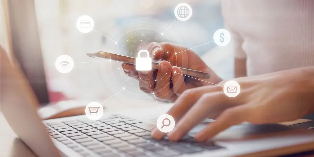 2 Hände vor einem Laptop, eine Hand hält ein Handy, vom Handy aus sind Symbole dargestellt die die Sicherheit beim surfen und einkaufen symboliiseren