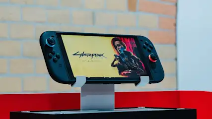 Nintendo Switch 2 Handheld-Konsole mit schwarzem Gehäuse steht auf einem Ständer und zeigt das Spiel Cyberpunk 2077 Ultimate Edition auf dem Display.