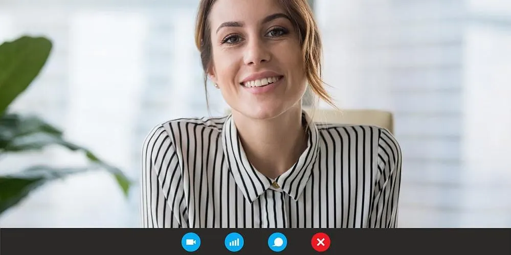 Frau in gestreifter Bluse sitzt bei einem Videotelefonat vor einem unscharfen Hintergrund. Unten im Bild sind die Symbole einer Videochat-Software sichtbar.