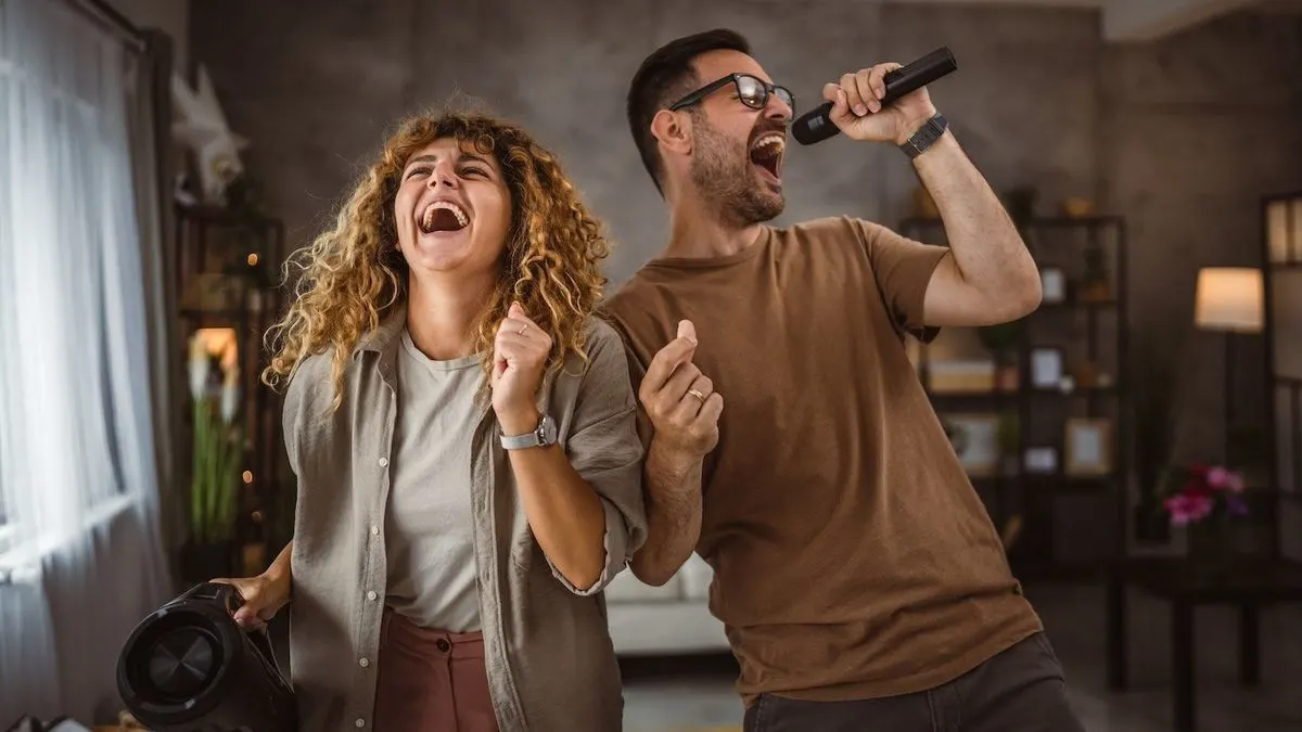 Eine lachende Frau mit Bluetooth Lautsprecher und ein singender Mann mit Mikrofon.