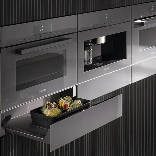 Graue Küche mit eingebauten Geräten. Eine Schublade ist geöffnet und enthält eine Schale mit Speisen.