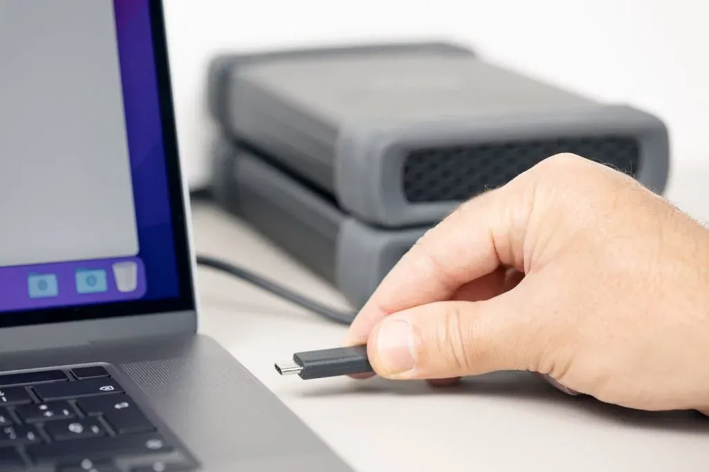 Hand steckt USB‑C‑Kabel in Laptopanschluss, im Hintergrund zwei externe Festplatten.
