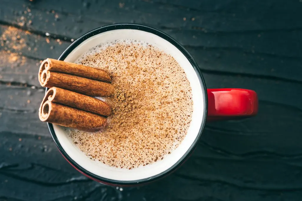 Tasse mit Milchschaum und Zimtstangen auf schwarzem Holz.