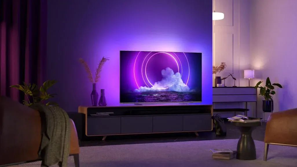 TV mit lila Ringen und Wolken, lila Umgebungsbeleuchtung. Holz-TV-Möbel, Pflanzen, Sessel und Beistelltisch im Wohnzimmer.