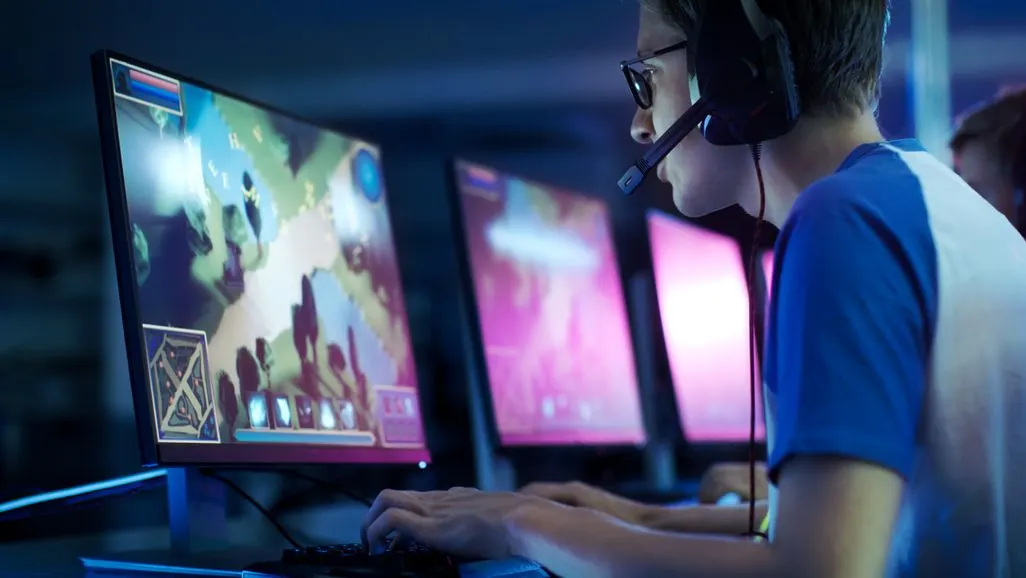 Ein Jugendlicher sitzt vor einem Bildschirm mit Computerspiel und trägt ein Headset.