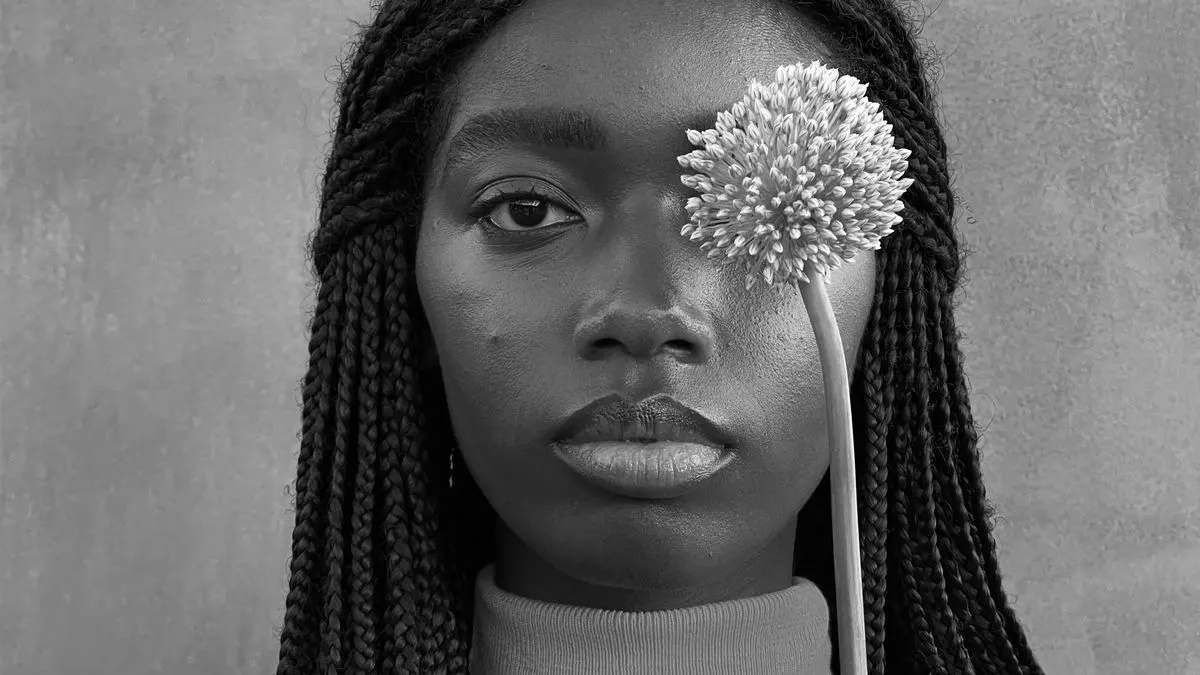Eine Person mit langem geflochtenen Haar mit einer Blüte vor einem Auge
