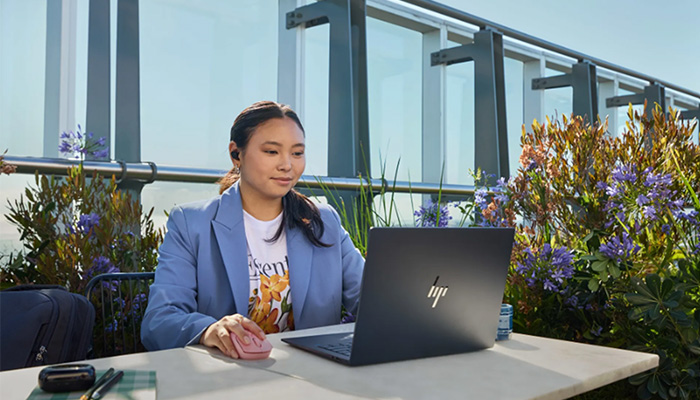 Eine Frau sitzt auf einem Tisch und arbeitet mit einem HP Notebook