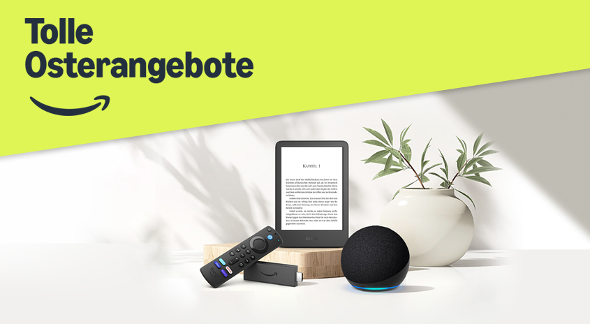 Ein E-Reader, eine Fernbedienung, ein Streaming-Stick und ein Echo Dot stehen vor einer Vase mit Pflanzen auf einem Tisch.