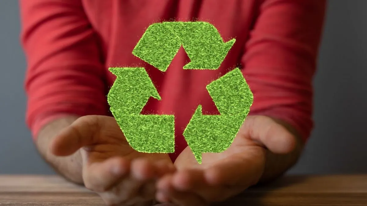 Person in rotem Shirt haelt das Recycling Symbol aus gruenem Kunstgras in den Haenden