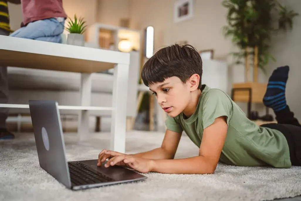 Bub liegt auf dem Teppich und tippt konzentriert auf einem Laptop im Wohnzimmer.