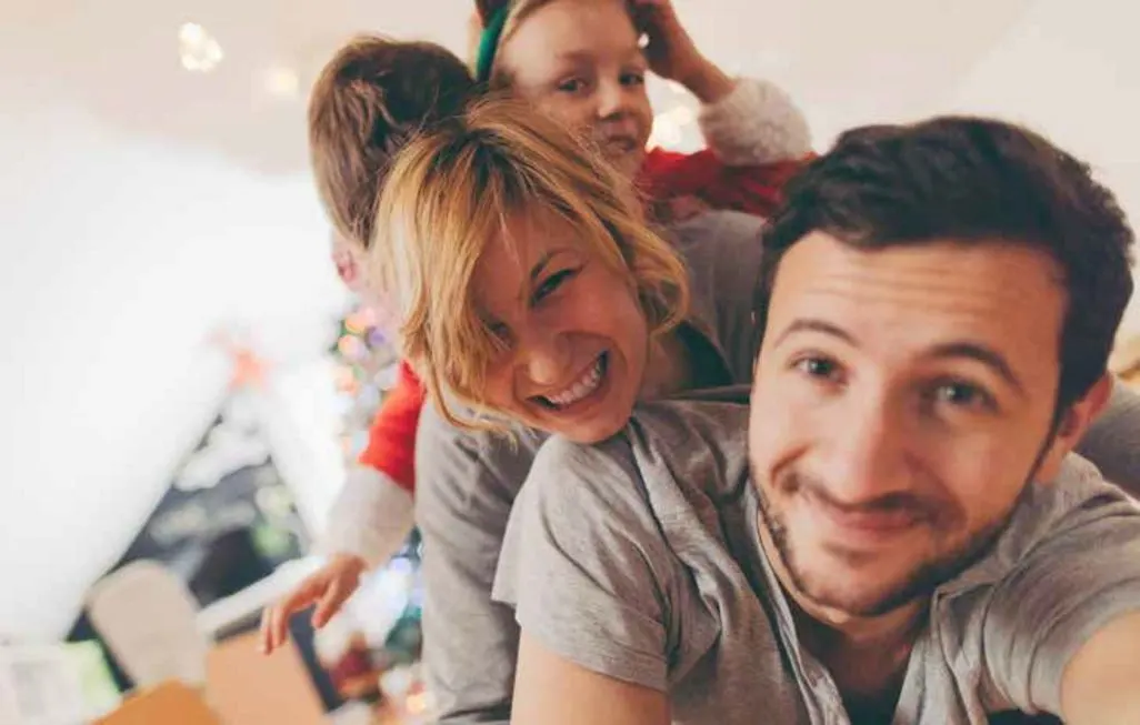 Familie liegt zusammen auf dem Boden vor einem Weihnachtsbaum.