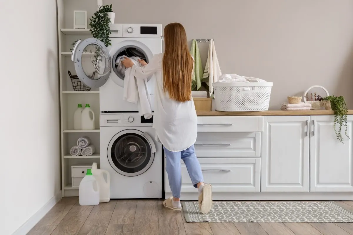 Eine Frau mit langen blonden Haaren befüllt einen Trockner der auf einer Waschmaschine steht.