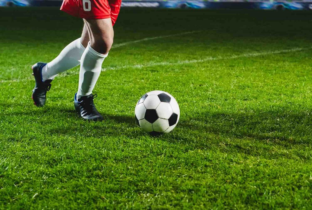 Fußballspieler Nummer 8 im roten Trikot dribbelt einen schwarzweißen Ball auf grünem Rasen während eines Stadionpiels.