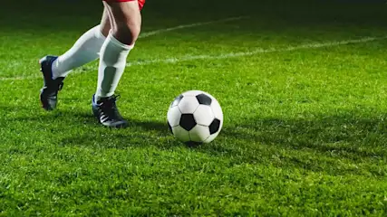 Fußballspieler Nummer 8 im roten Trikot dribbelt einen schwarzweißen Ball auf grünem Rasen während eines Stadionpiels.