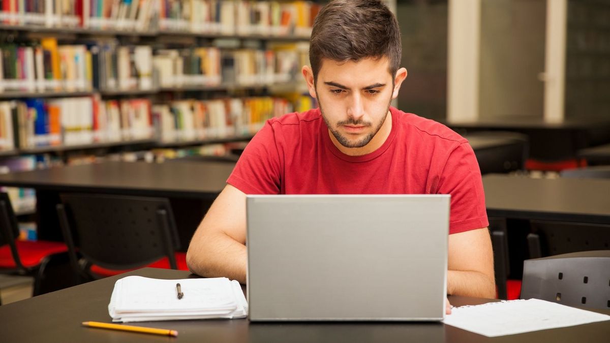 Ein Mann arbeitet fokussiert am Laptop in einer Bibliothek.