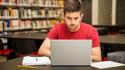 Ein Mann arbeitet fokussiert am Laptop in einer Bibliothek.