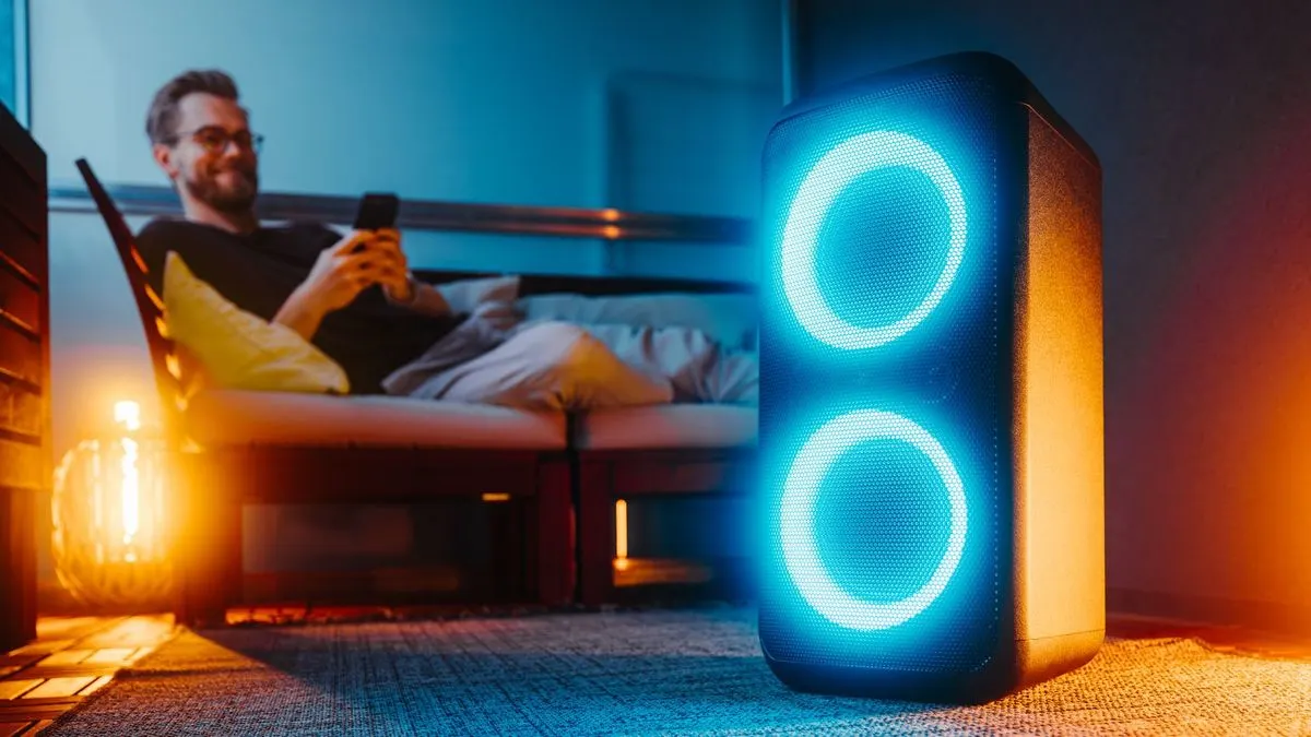 Leuchtende Partybox wird von einem Mann am Sofa mit einem Smartphone gesteuert.